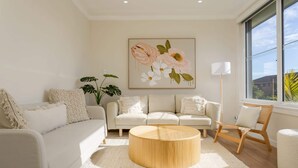 A modern living room with a white sofa, a round wooden coffee table, and a large window with a view of the sky.