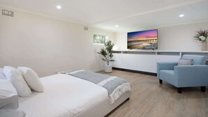 A modern bedroom with a bed, a blue armchair, a TV, and a plant.