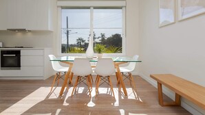 A modern kitchen with white cabinets, a built-in oven, and a glass dining table with white chairs.