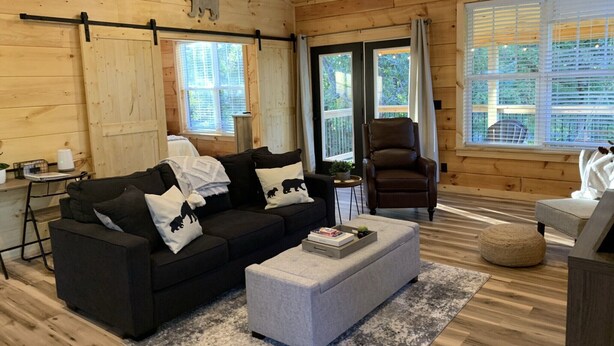 Una habitación acogedora de estilo cabaña con un sofá negro, un reposapiés gris y un sillón de cuero marrón.