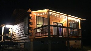 Una cabaña de madera de dos pisos con un balcón y luces colgantes.