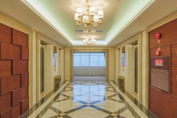 A hotel corridor with a geometric patterned floor, a chandelier, and a red emergency exit sign. - Taishan Gaoye Hotel (Taishan)