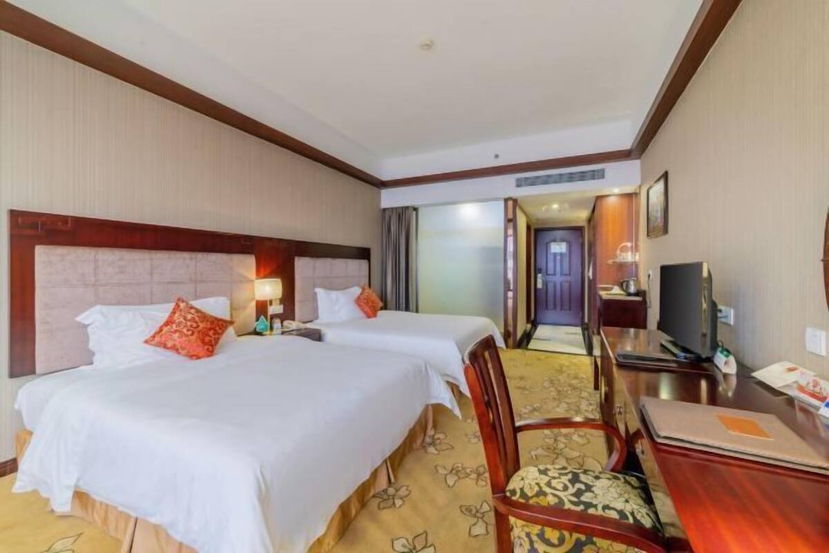 Una habitación de hotel con dos camas, un escritorio, una silla y un televisor.