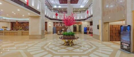 Un vestíbulo amplio con una planta ornamental central, una recepción y un diseño de techo moderno.