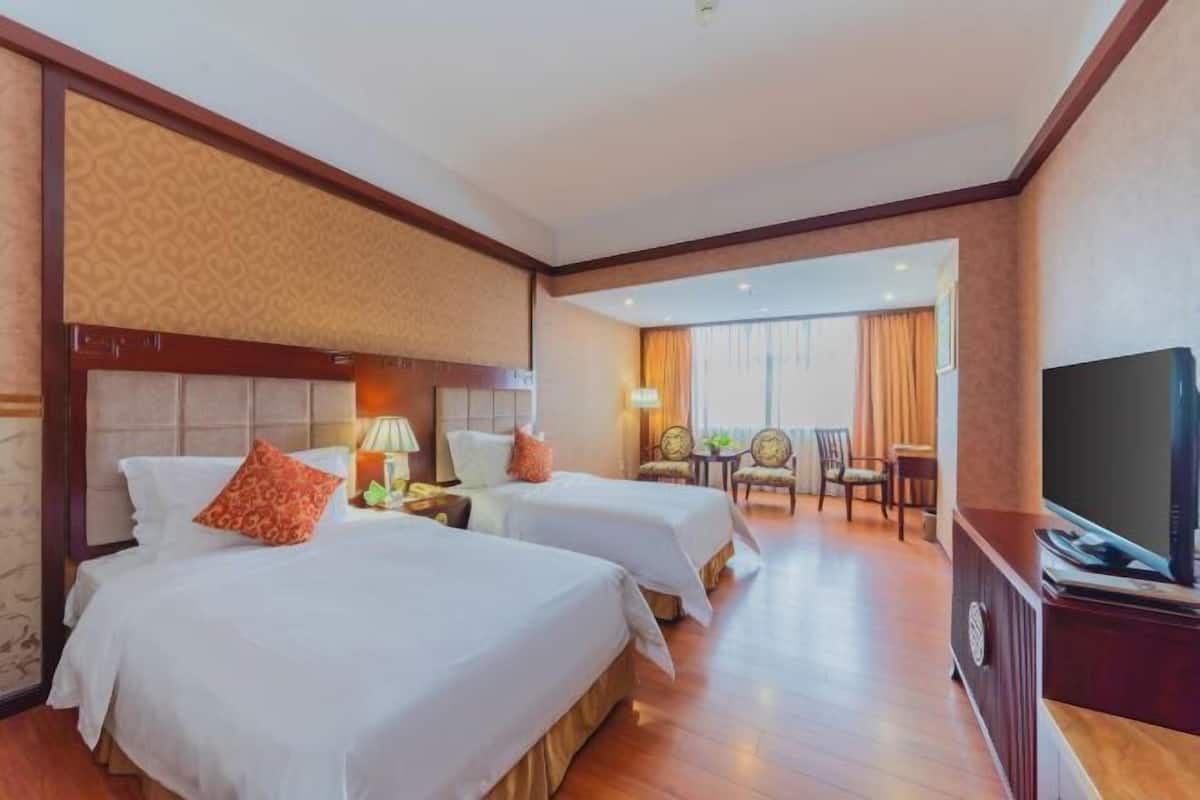 Habitación de hotel con dos camas, televisor, escritorio y zona de comedor con sillas.
