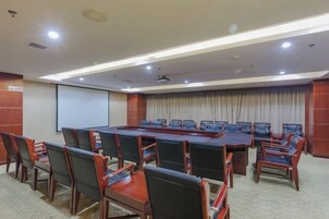 Un salón de conferencias con una larga mesa y sillas, una pantalla de proyector y suelo alfombrado.