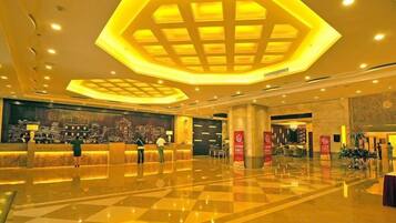 A hotel lobby with a check-in counter, a large illuminated geometric ceiling design, and a polished floor.