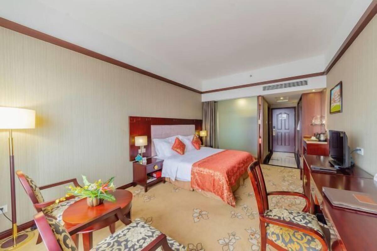 Habitación de hotel con cama, escritorio, silla, lámpara y televisor.