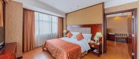A hotel room with a large bed, a TV, a nightstand, and a door leading to another room.