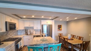 A modern kitchen with white cabinets, stainless steel appliances, and a dining area with wooden chairs and a table.