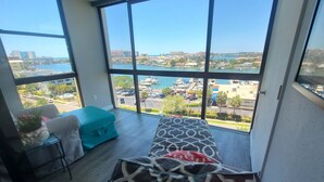 A balcony with a bed, a small table with a plant, and a view of a marina and buildings.