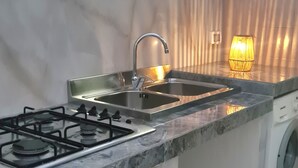 Una cocina con estufa a gas, pileta de acero inoxidable y lavadora.