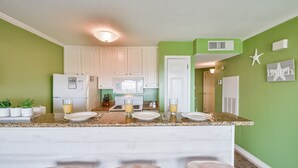 A kitchen with white cabinets, a granite countertop, and a bar area with stools. - Pool Views, Good Times and Beach Vibes at Sea Breeze! (Galveston)