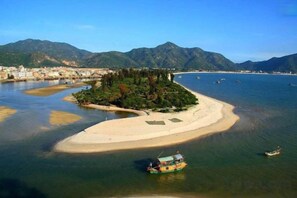 A coastal landscape with a small island, boats, and a distant shoreline with buildings. - Huizhou Kaixuan Yuntian Hotel (Chenjiang Branch) (Huizhou)
