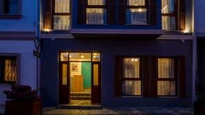 Un edificio de dos pisos con entrada a nivel de calle, varias ventanas con contraventanas y una puerta visible que da al interior.