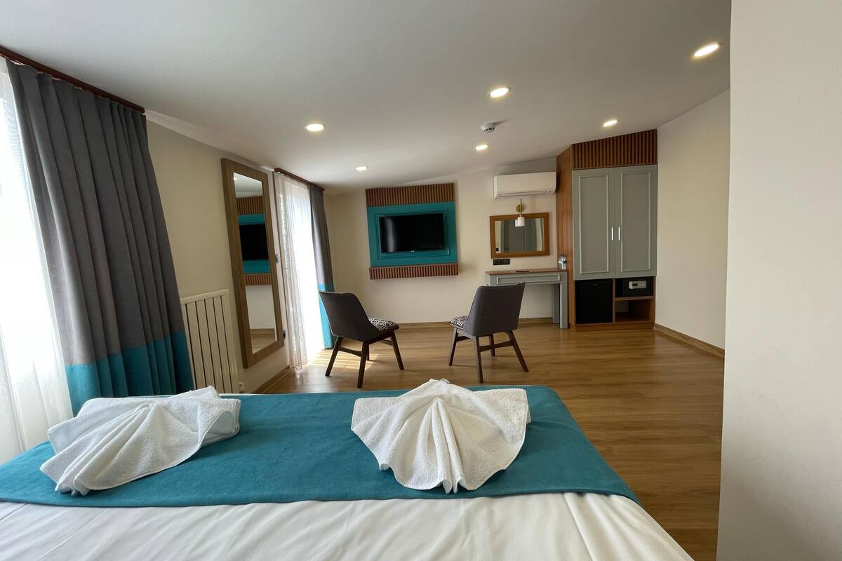 A hotel room with a bed, two chairs, a desk, a TV, and a wardrobe.