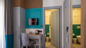 Una habitación compacta con una pared de acento color turquesa, una kitchenette, una silla gris y una puerta que conduce a un baño.