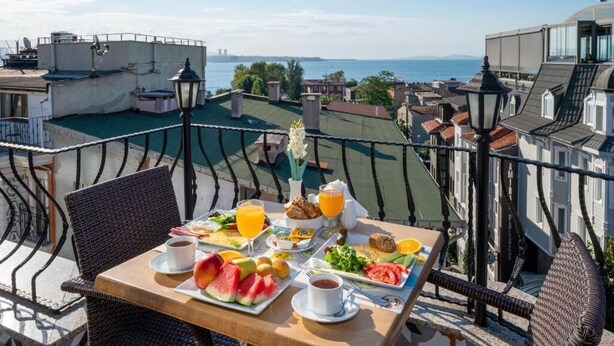Un balcón con una mesa lista para el desayuno, con vistas a la ciudad y al mar.