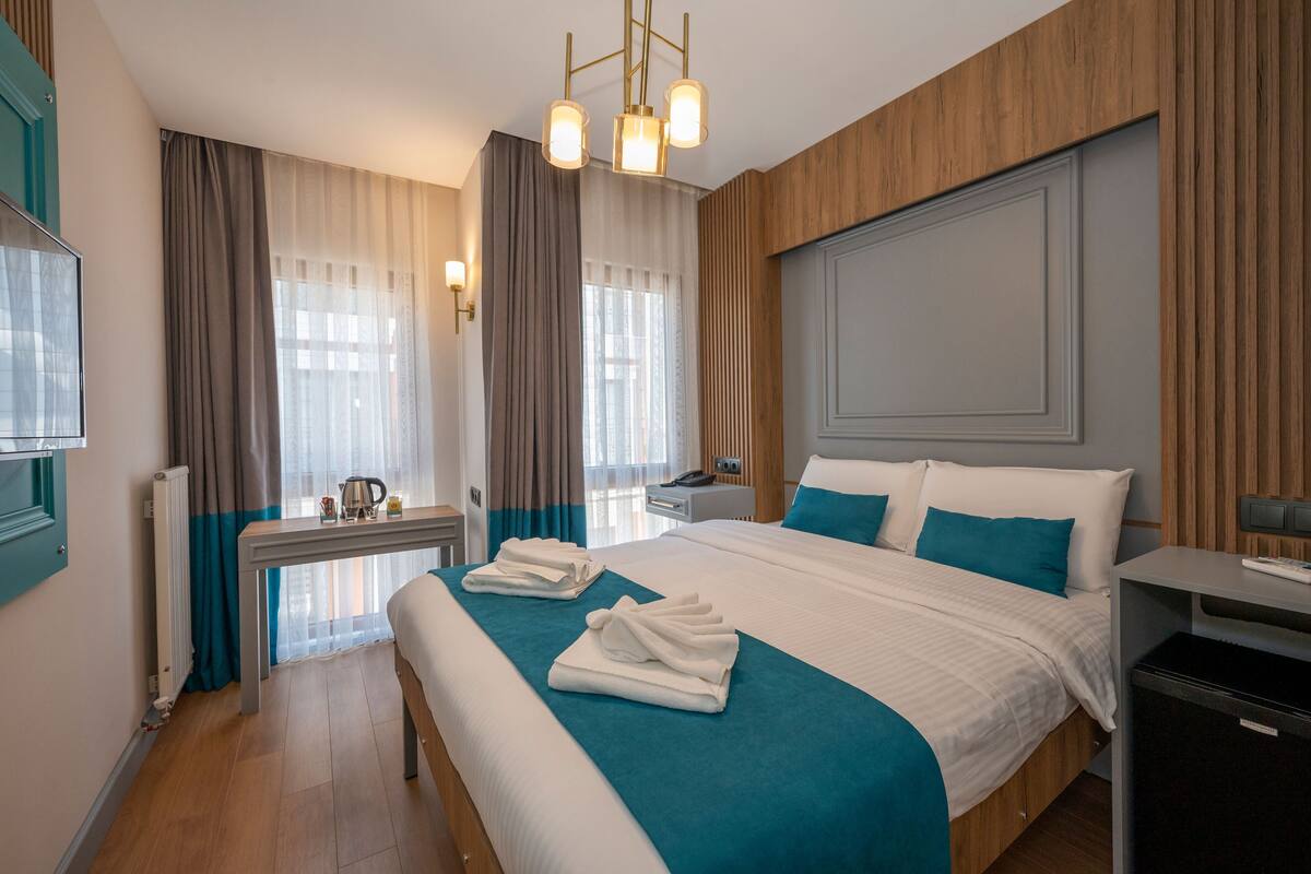 A hotel room with a large bed, a bedside table, a desk, and a chair.