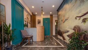 Un vestíbulo con una puerta verde azulado, un mostrador de recepción, una silla estampada y un mural de un árbol y una hamaca.