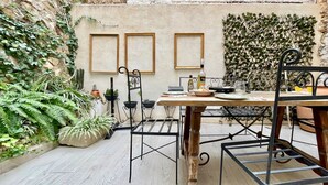 A rustic outdoor dining area with a wooden table and metal chairs, surrounded by potted plants and a textured wall. - Village house with patio (Altea)