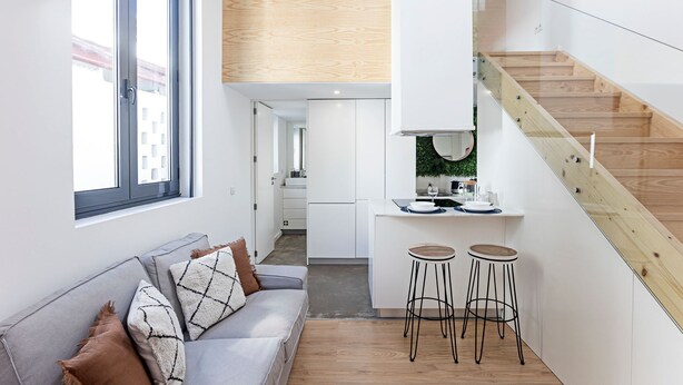 Et moderne køkken med hvide skabe, en trætrappe og en grå sofa med puder.