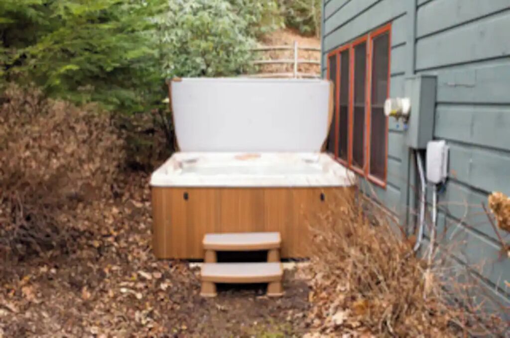 A hot tub in a backyard with a wooden deck and steps leading up to it.
