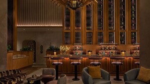 A bar area with multiple stools, a bar counter, and a large wine rack in the background. - Moxy Brooklyn Williamsburg (Brooklyn)
