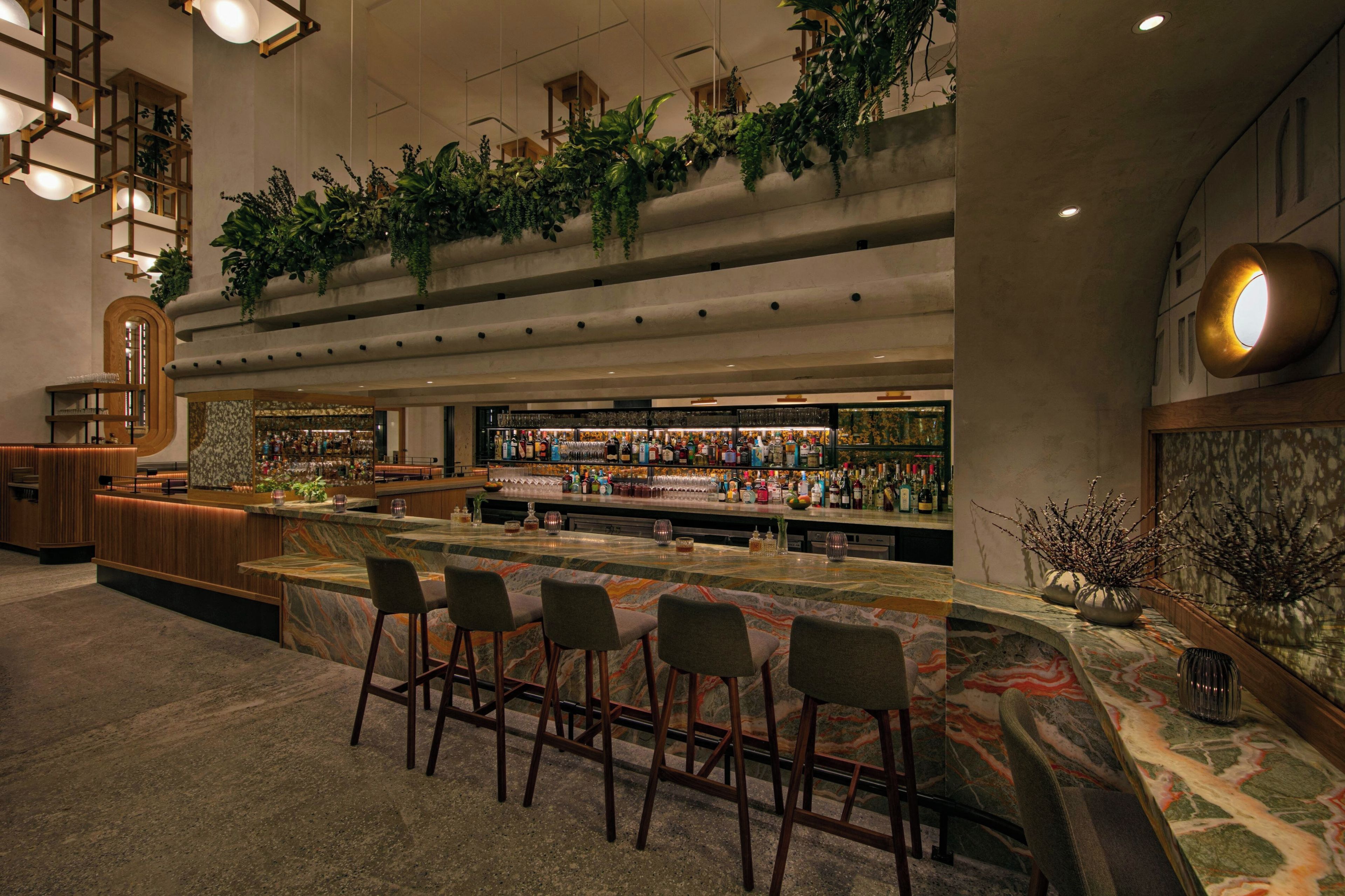 A bar area with a marble countertop, bar stools, and a variety of bottles and glasses.