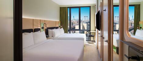 Habitación de hotel con dos camas, un ventanal grande con vista a la ciudad, televisión y baño con espejo y lavamanos.