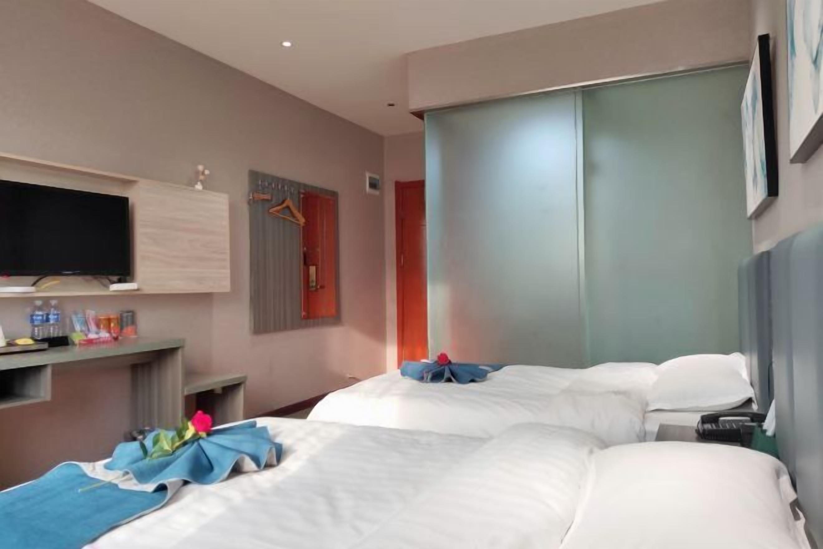 A hotel room with two beds, a flat-screen TV, a minibar, and a sliding door closet.