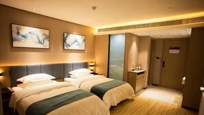 Ein Hotelzimmer mit zwei Betten, einem Nachttisch, einem Schreibtisch mit Stuhl und einer Badezimmertür.