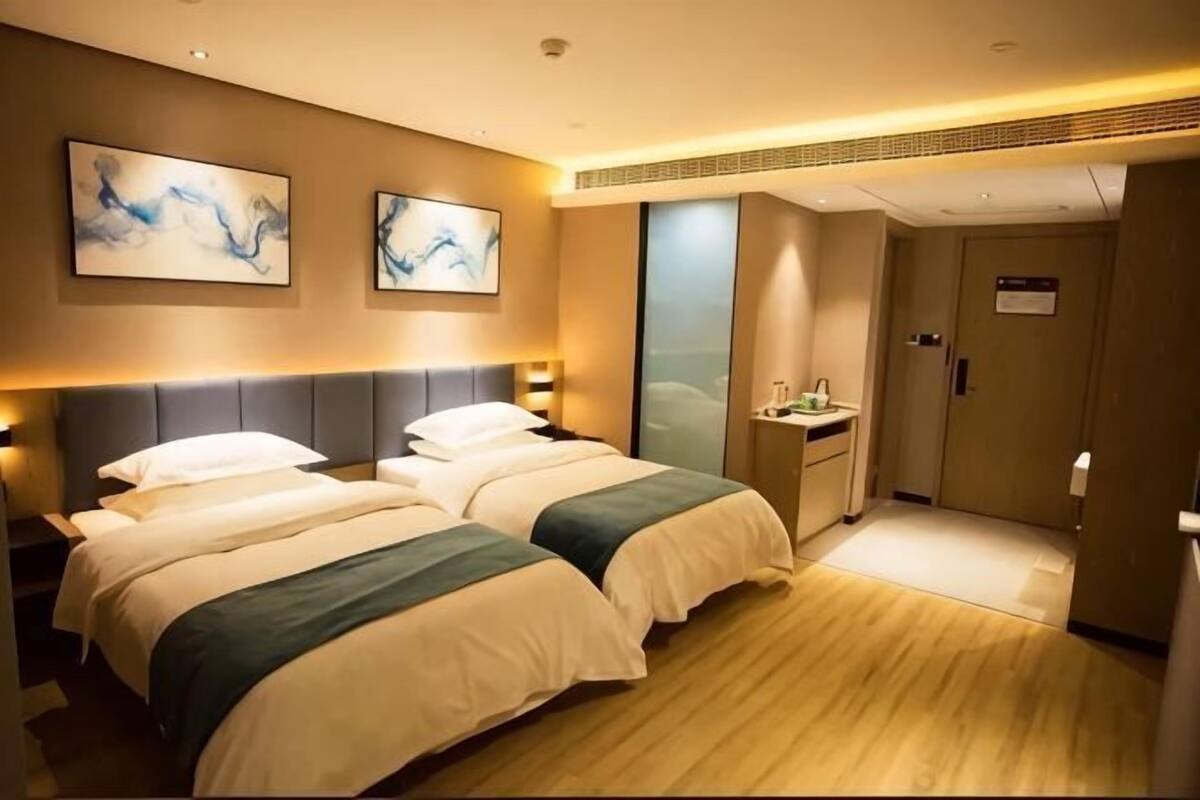 Habitación de hotel con dos camas, una mesita de noche, un escritorio con silla y la puerta del baño.