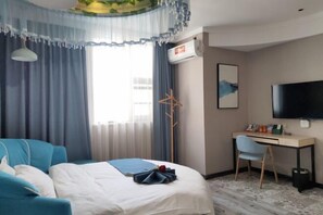 Habitación de hotel con cama, escritorio, silla, televisor y ventana con cortinas.