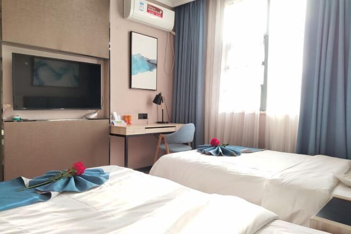 Habitación de hotel con dos camas, un escritorio, un televisor y una ventana con cortinas.