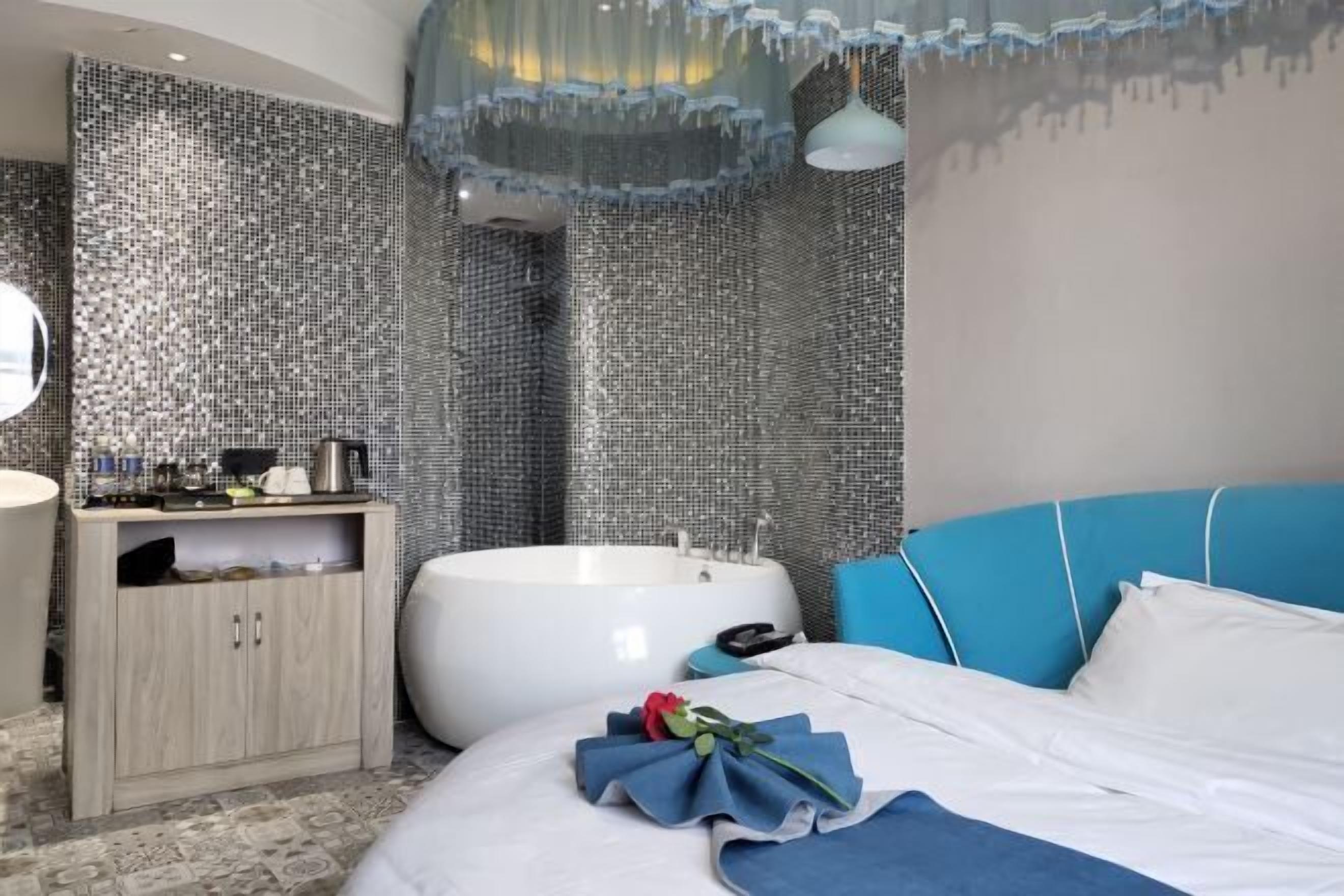 A modern bathroom with a large bathtub, a wooden cabinet, and a blue upholstered headboard.
