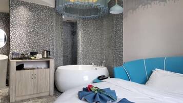 A modern bathroom with a large bathtub, a wooden cabinet, and a blue upholstered headboard.