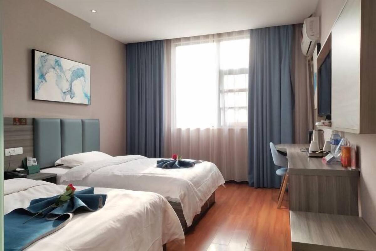 Una habitación de hotel con dos camas, un escritorio y un amplio ventanal con cortinas.