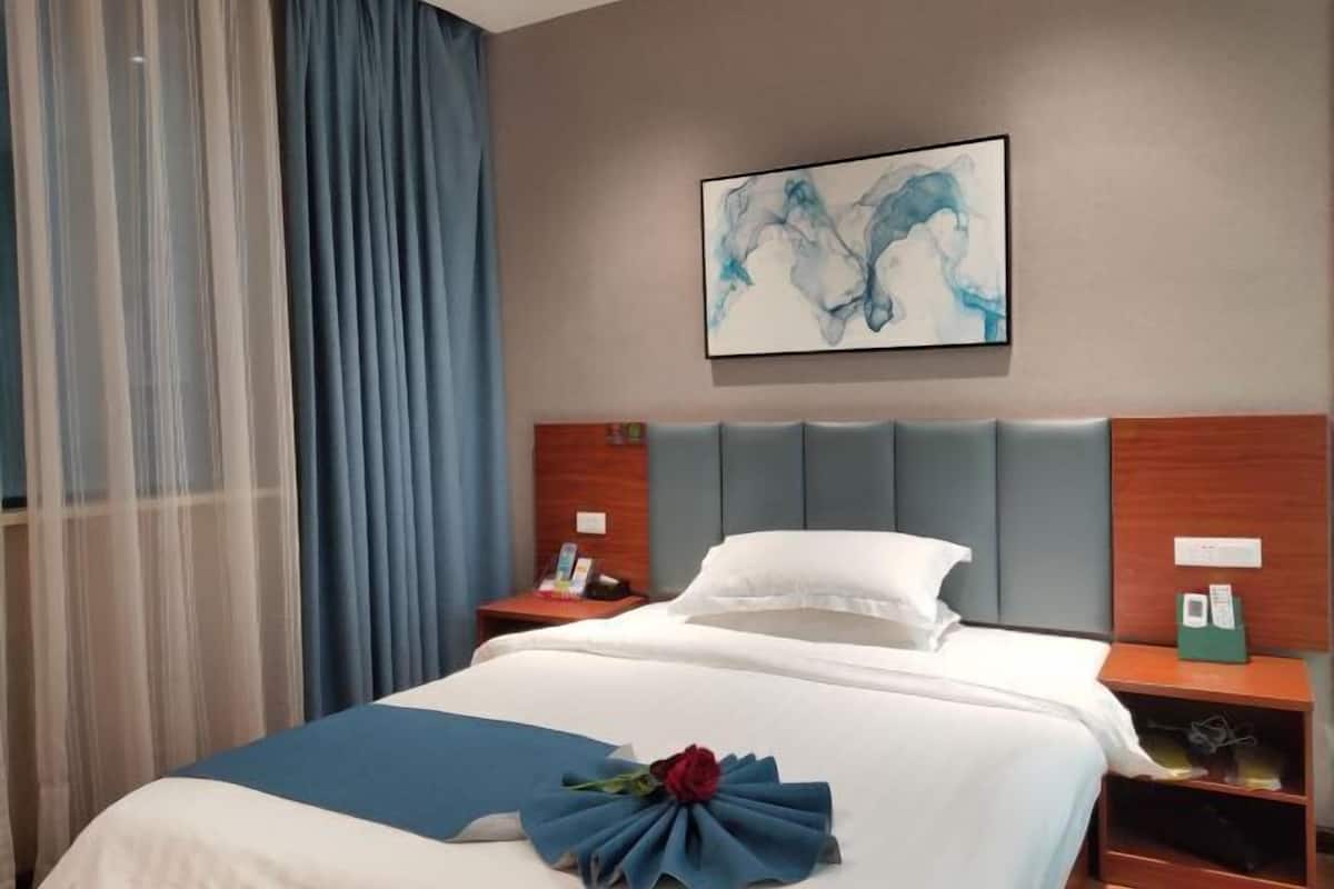 Habitación de hotel con cama, cabecera, mesita de noche, una obra de arte colgada en la pared y ventana con cortinas.