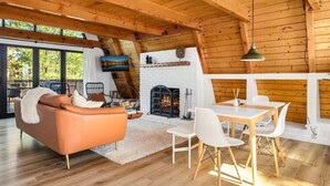 Un salon chaleureux avec une cheminée, des poutres apparentes en bois au plafond, un canapé et un coin repas avec des chaises.