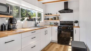 Une cuisine moderne avec des armoires blanches, un plan de travail en bois, un four encastré et une fenêtre laissant entrer la lumière naturelle.