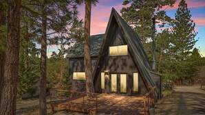 Une cabane moderne en bois, dotée d’un toit à forte pente, de grandes fenêtres et d’une terrasse en bois.