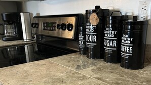 A kitchen counter with a stove, coffee maker, and four containers labeled with different contents. - Cozy Cowboy Condo (Paradise Valley)