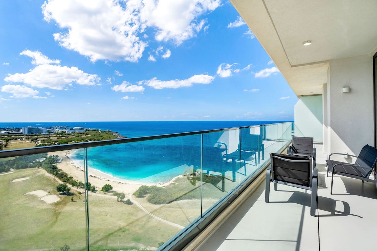 Un balcon doté d’une balustrade en verre, offrant une vue sur une plage et l’océan.