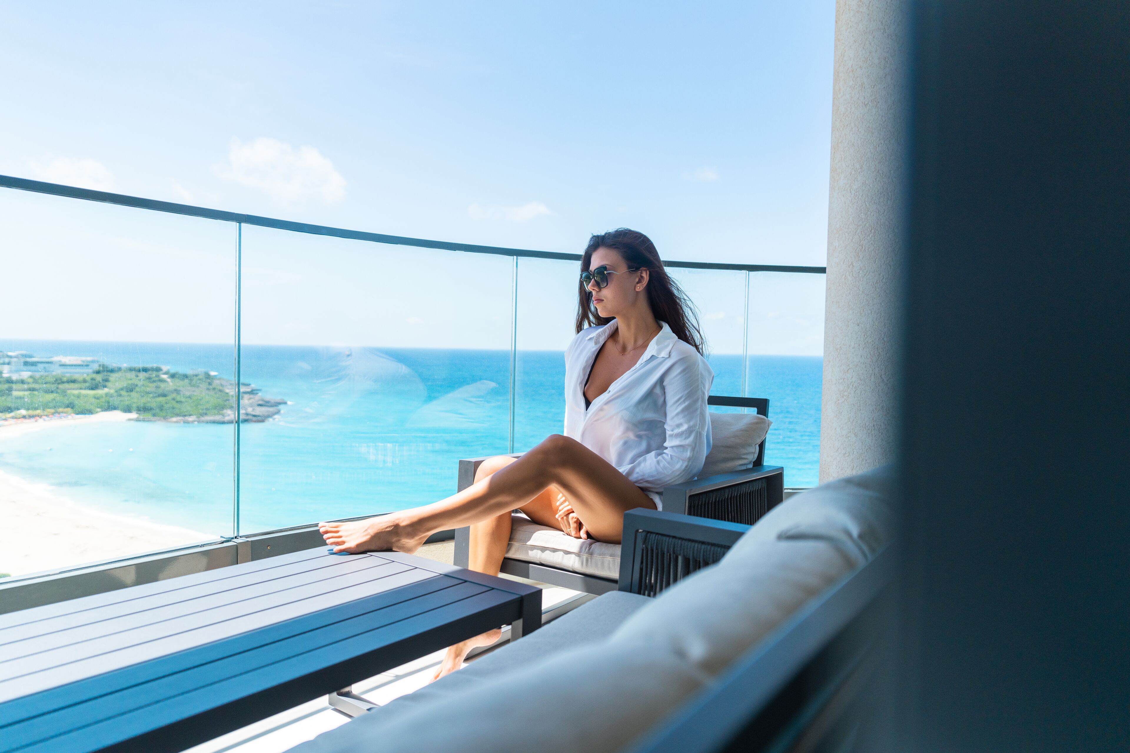 A person sitting on a balcony with a view of the ocean and a beach.