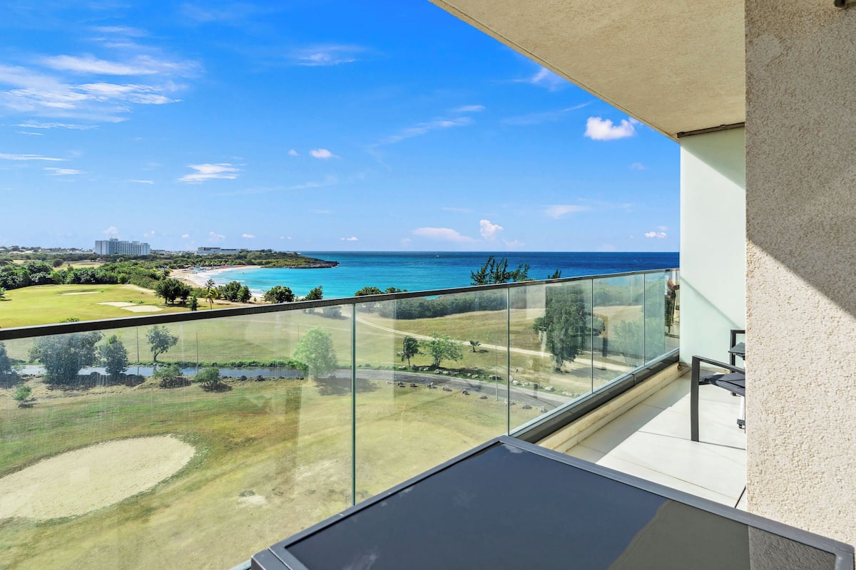Un balcon offrant une vue dégagée sur un terrain de golf, l’océan et les bâtiments situés au loin.