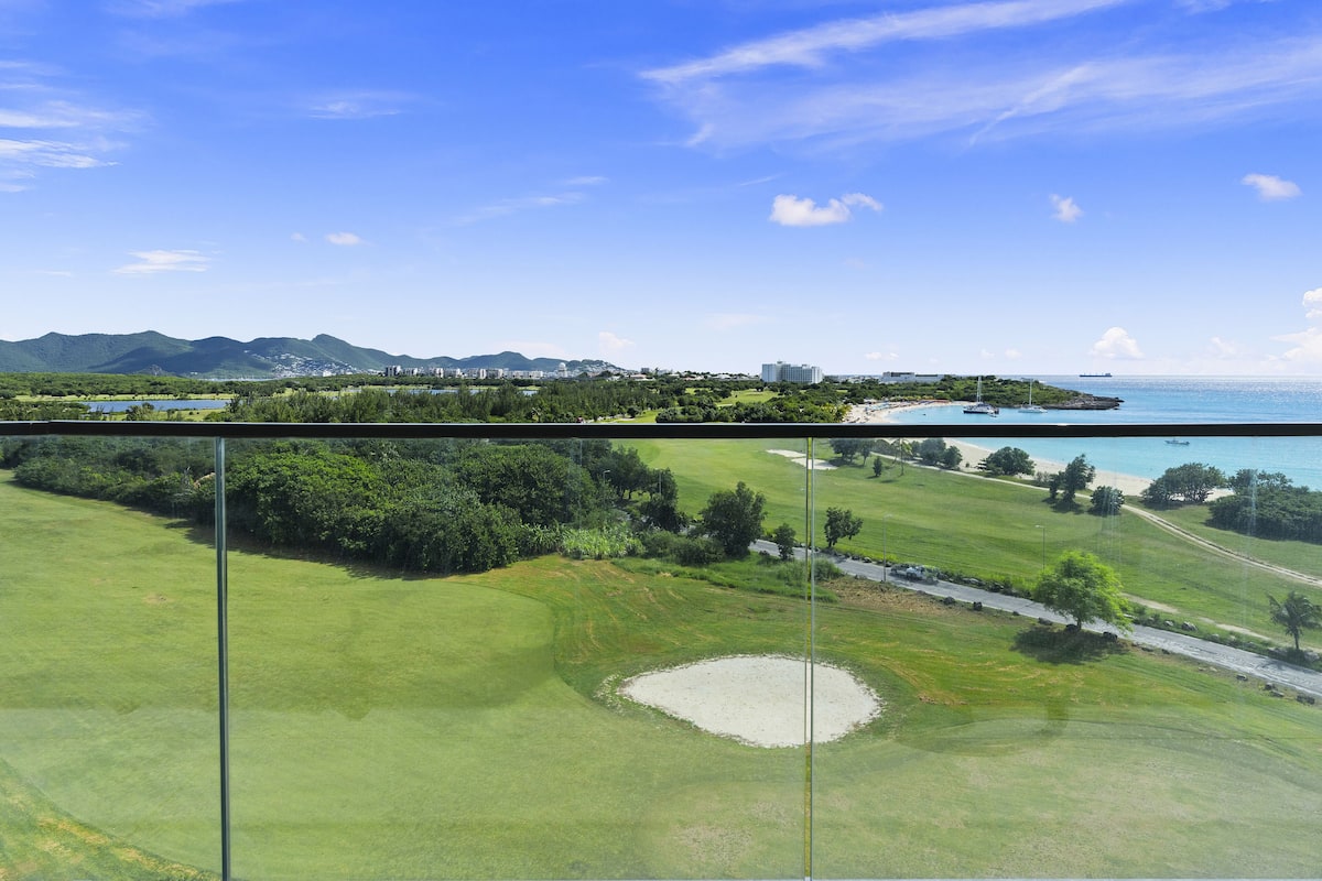 Un parcours de golf offrant une vue dégagée sur l’océan et les montagnes lointaines.