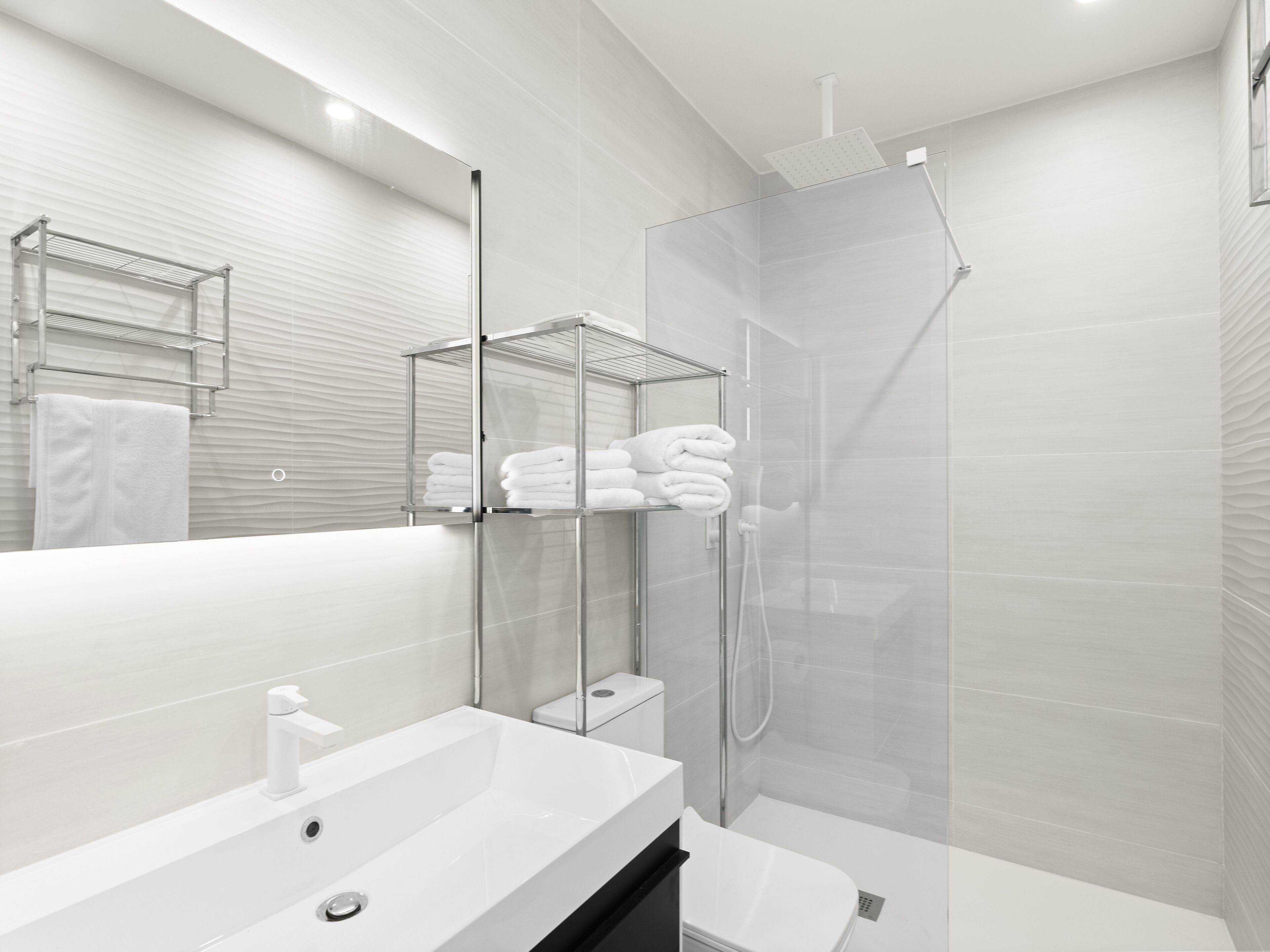 Een moderne badkamer met een douchecabine van glas, een wit wastafelmeubel en een toilet.