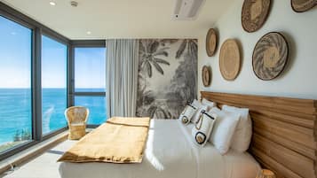 A bedroom with a large bed, a view of the ocean, and tropical-themed wall decor.