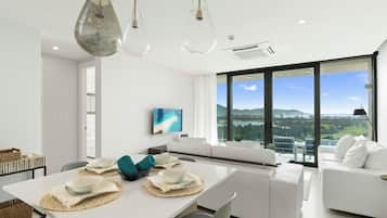 A modern dining area with a white table set for four, a large window with a city view, and a white sofa in the background.